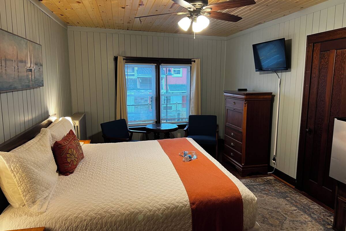 Habitación de hotel con cama, escritorio, silla, televisor y armario.