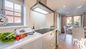 Une cuisine moderne dotée d’une cuisinière intégrée, d’une fenêtre avec des rideaux et d’un coin repas avec des chaises.