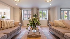 Un salon moderne avec deux canapés, une table basse ornée d’un vase de fleurs et de grandes fenêtres avec des rideaux.