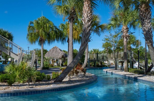 Relax by the serene pool surrounded by lush palm trees and a thatched-roof cabana.