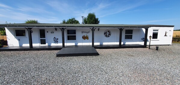 A white mobile home with a gravel driveway, a front porch, and decorative artwork.