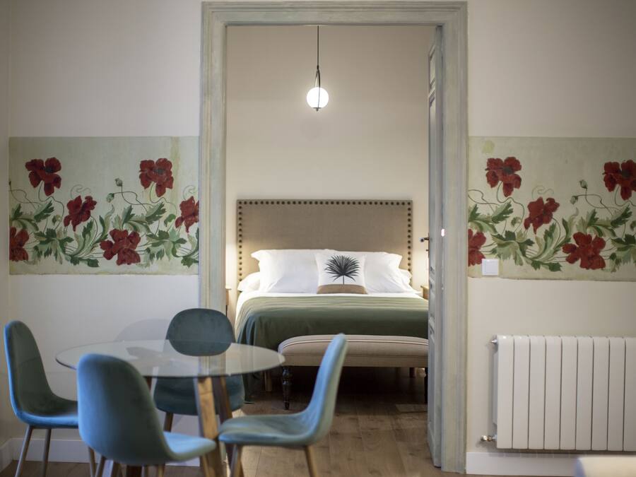 Un dormitorio con cama, una mesa y sillas, y decoración floral en la pared.