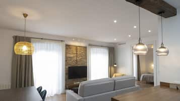 Ein modernes Wohnzimmer mit Holzboden, einem grauen Sofa, einem Esstisch mit Stühlen und Pendelleuchten.