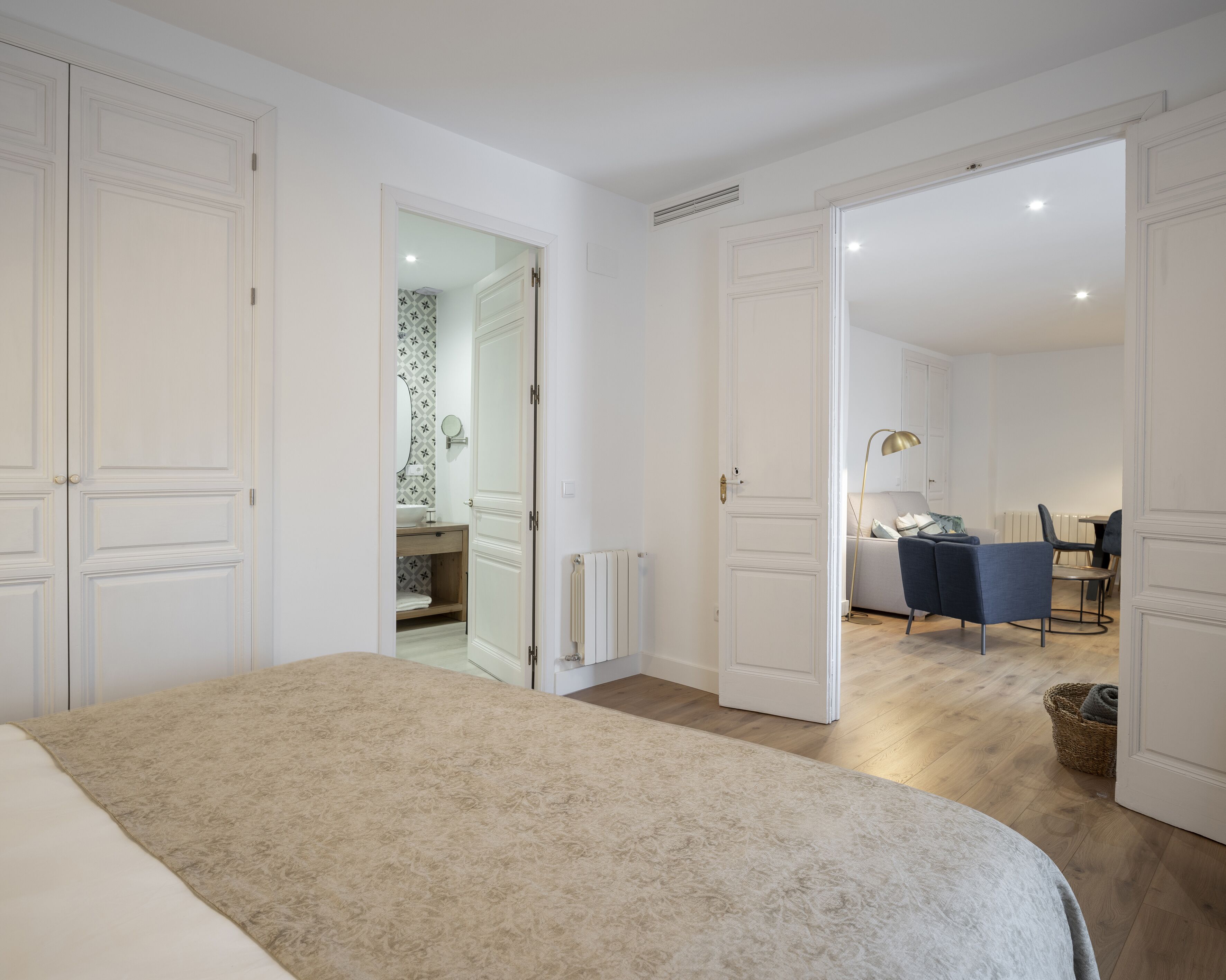 A bedroom with a bed, a bathroom with a mirror and sink, and a dining area with chairs and a table.