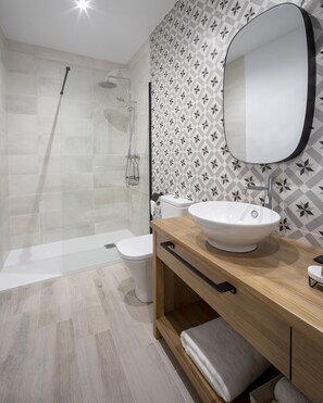 A modern bathroom with a glass-enclosed shower, a white toilet, and a wooden vanity with a large mirror.