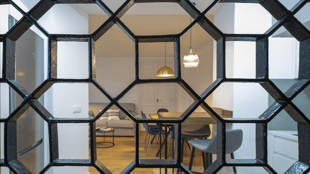 A modern interior with a geometric black metal partition, a sofa, a dining table, and chairs.