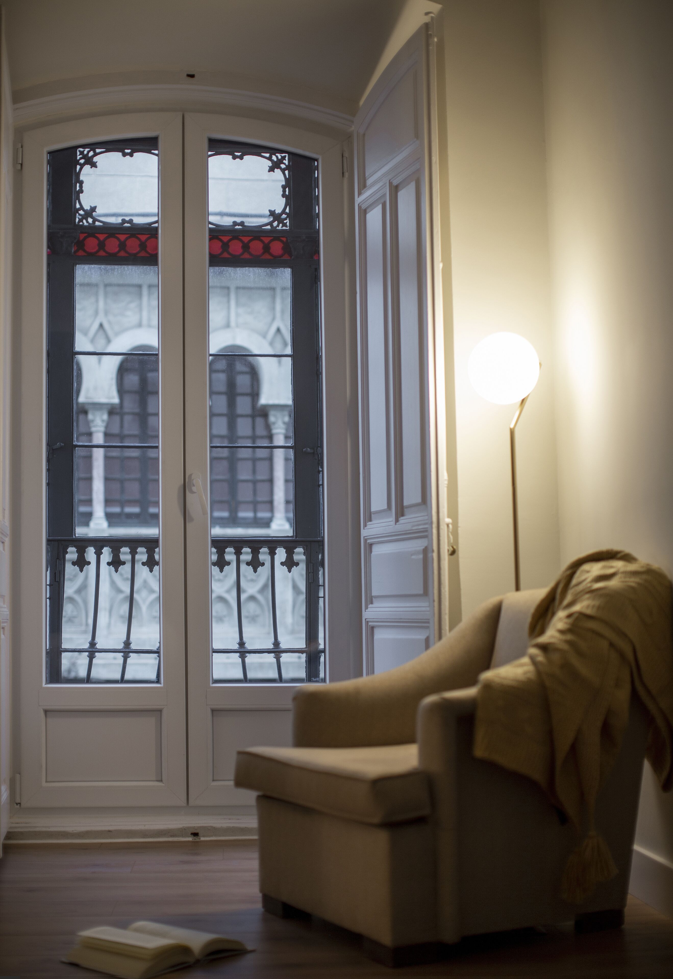 Una habitación con puerta que da a un balcón, una silla y una lámpara de pie.