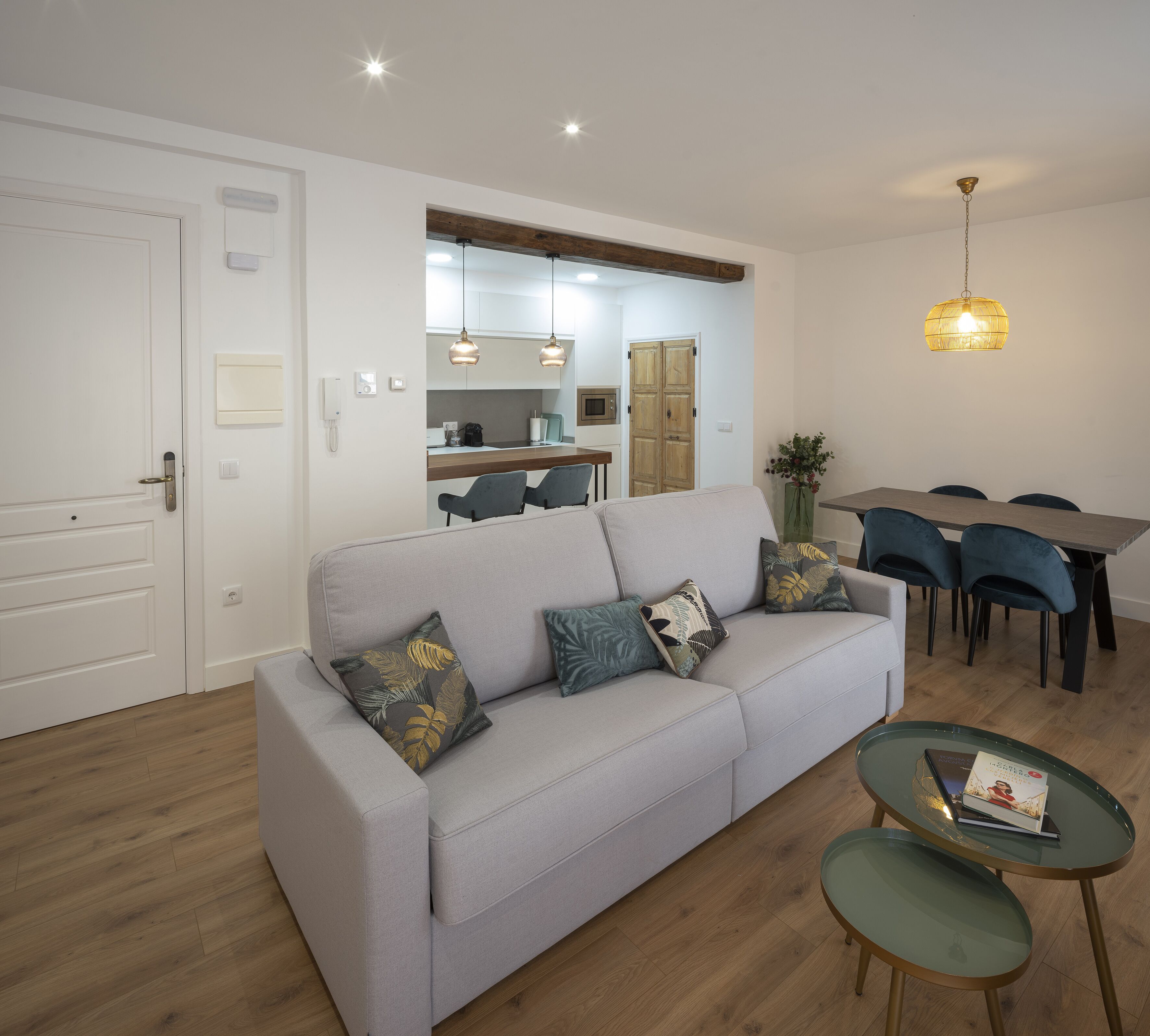 A modern living room with a grey sofa, a dining table with chairs, and a kitchen area in the background.