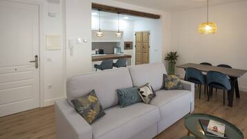 A modern living room with a grey sofa, a dining table with chairs, and a kitchen area in the background.