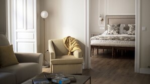 A modern living room with a sofa, armchair, and coffee table. A bed is visible in the background.