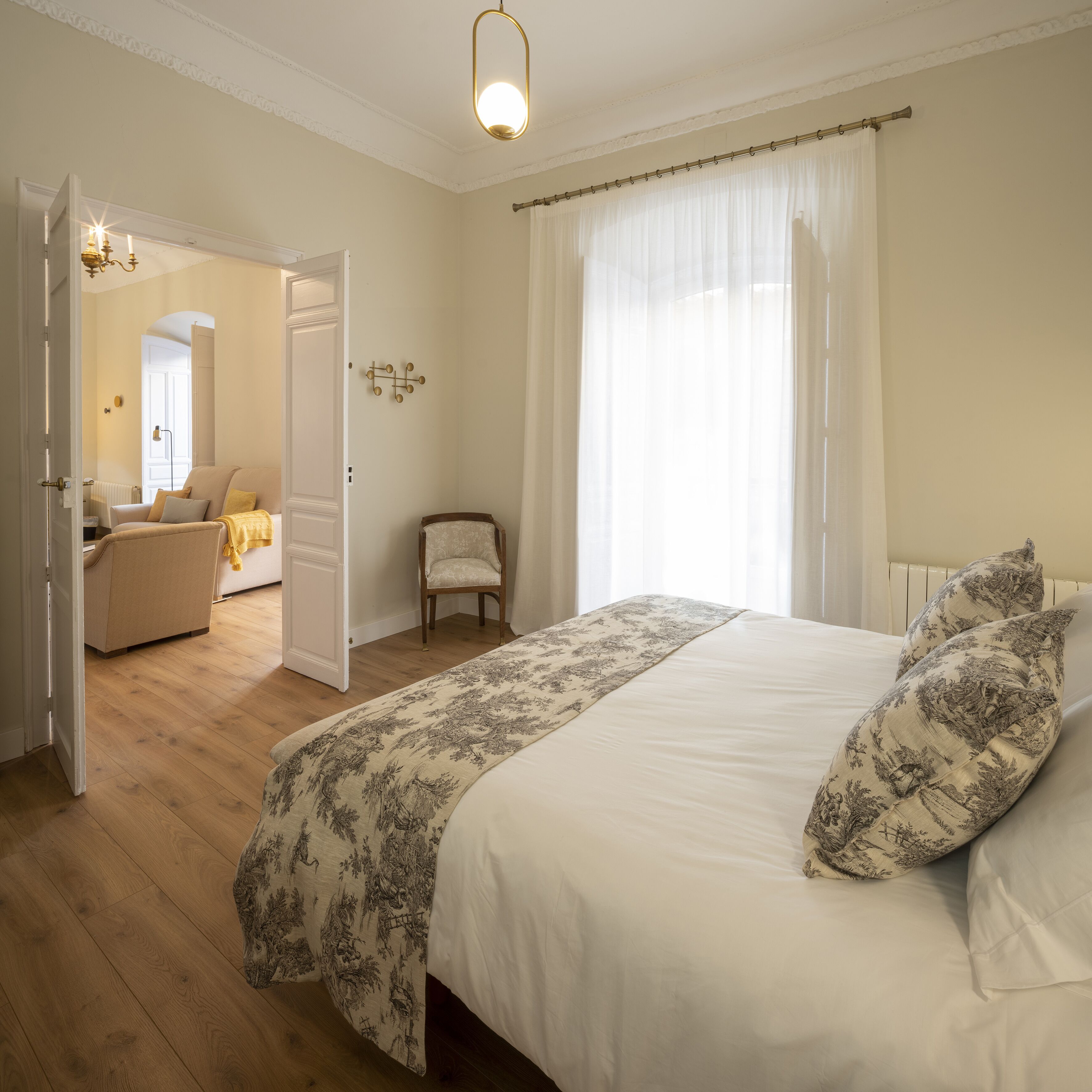 A bedroom with a large bed, a chair, and a door leading to another room.