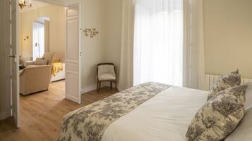A bedroom with a large bed, a chair, and a door leading to another room.