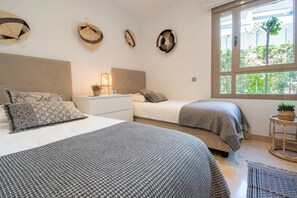 Un dormitorio con dos camas, una mesita de noche con lámpara y una ventana que da a zonas verdes.