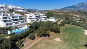 Un hotel moderno con varios balcones, una piscina y un campo de golf al fondo.