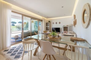 Una sala de estar moderna con una mesa de comedor de vidrio, sillas blancas, un sofá y un televisor.