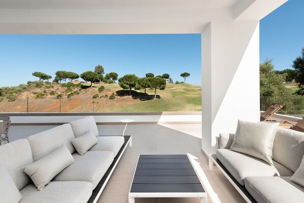 Un área de estar moderna al aire libre con vistas a una colina cubierta de hierba y árboles.