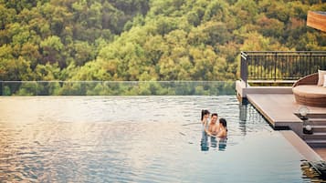 A couple in a clear infinity pool with a view of a forested hillside.