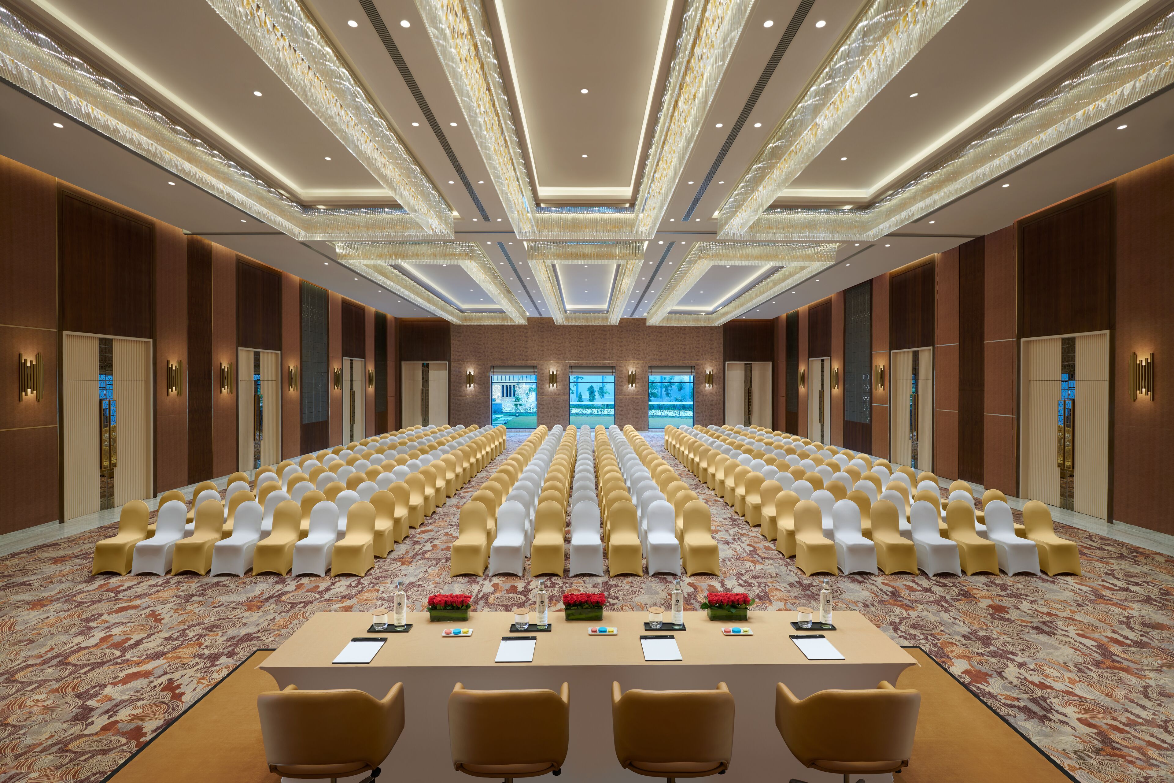 A conference room with rows of chairs, a long table with floral centerpieces, and a patterned carpet.