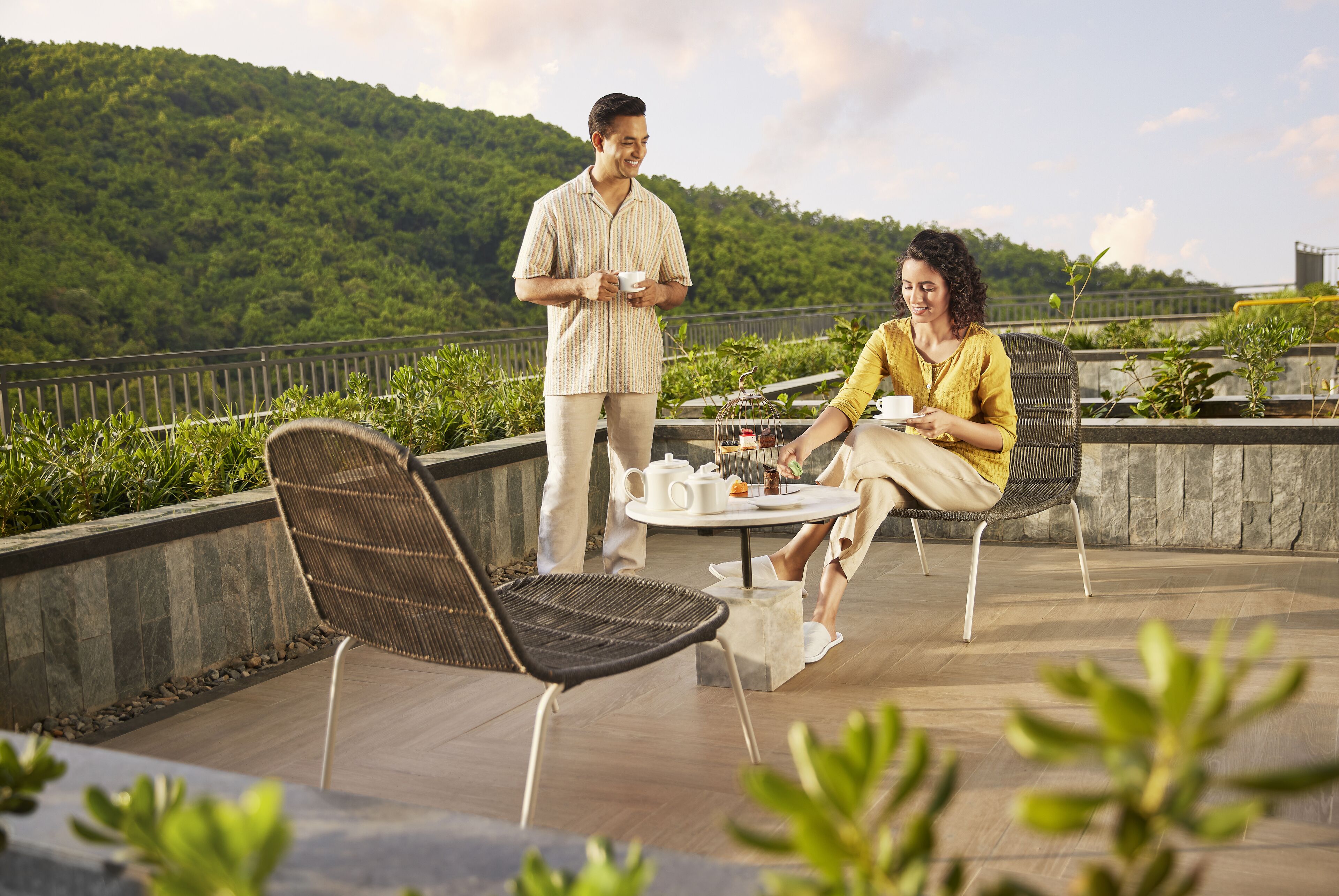 Un couple est assis à une table en plein air, avec une vue sur une colline verdoyante.