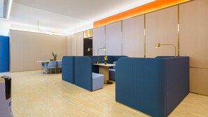 Un hall d’hôtel moderne, doté d’espaces de détente, d’un comptoir d’accueil et d’un mur décoratif agrémenté d’une bande lumineuse chaleureuse.
