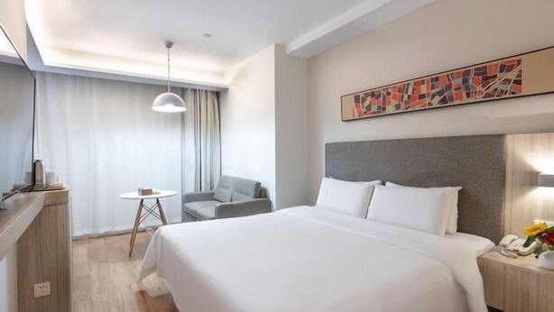 Une chambre d’hôtel moderne, dotée d’un grand lit, d’un bureau avec un téléphone, d’une petite table et d’une chaise.