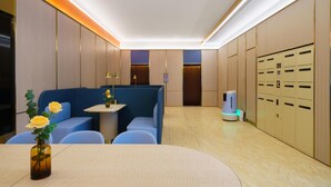 Un hall d’hôtel moderne avec un espace salon, une petite table agrémentée d’un vase de fleurs et un kiosque en libre-service.