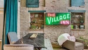 Ein gemütliches Interieur mit einem Neon-Schild, das "The Village Inn" zeigt, Ziegelwänden, einem Marmortisch und bequemen Sitzgelegenheiten.