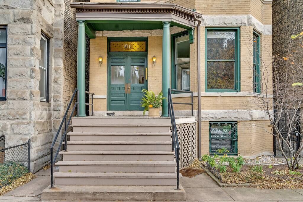 A building with a stone facade, green-framed windows, and a green door with a number plaque.
