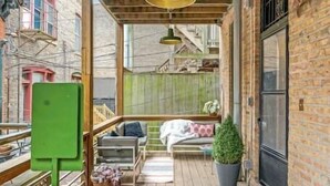 Ein überdachter Außenbereich mit Holzboden, einer grünen Bank, einem kleinen Tisch und einem Blumentopf.