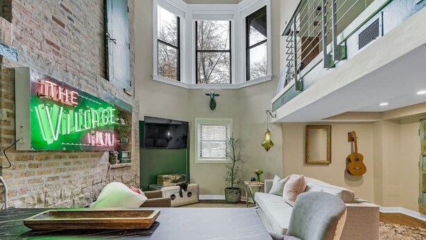 Ein gemütliches Wohnzimmer mit einer Neonreklame, einem Kamin, einem Fernseher und einer Gitarre.