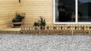 Fachada de madera con puerta corredera de vidrio, un pequeño espacio al aire libre con plantas y suelo de grava.