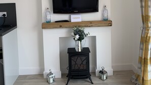 Una sala de estar moderna con un televisor montado, un reloj, una chimenea y un estante de madera con objetos decorativos.