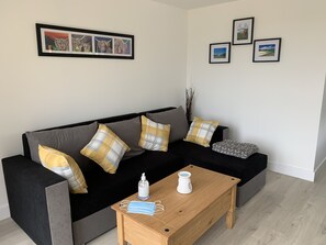 A modern living room with a black sofa, yellow and gray pillows, a wooden coffee table, and framed artwork on the wall.