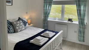 Un dormitorio con cama, mesita de noche, ventana con cortinas y radiador.