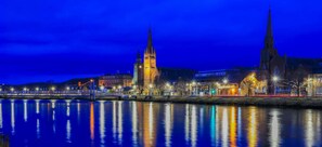 A nighttime cityscape with illuminated buildings and a river reflecting the lights. - Charming 2-bed Cabin in Inverness, Scotland (Inverness)