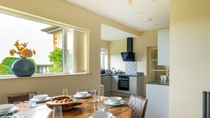 A dining area with a round table set for four, a kitchen in the background, and a window with a view of greenery. - 3 bedroom accommodation in Long Riston, near Beverley (Long Riston, near Beverley)