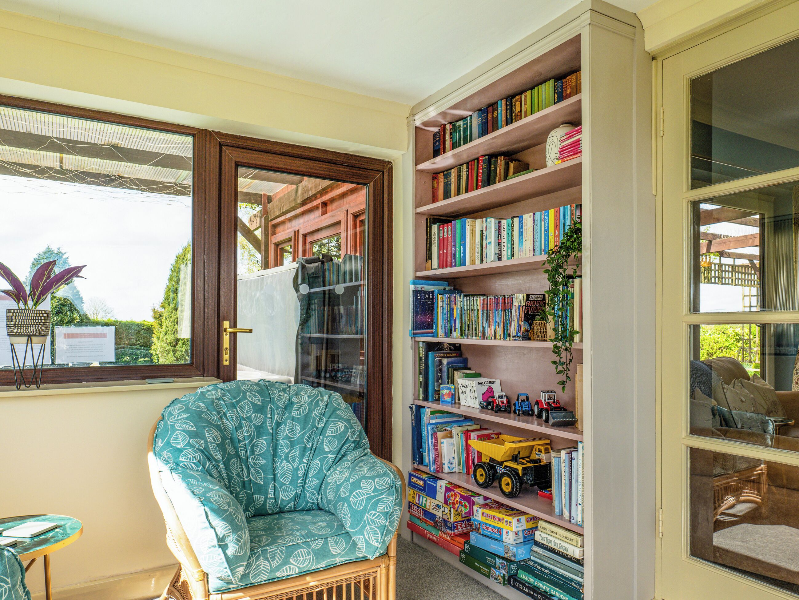 Une pièce avec une fenêtre, une chaise, une bibliothèque et une porte.