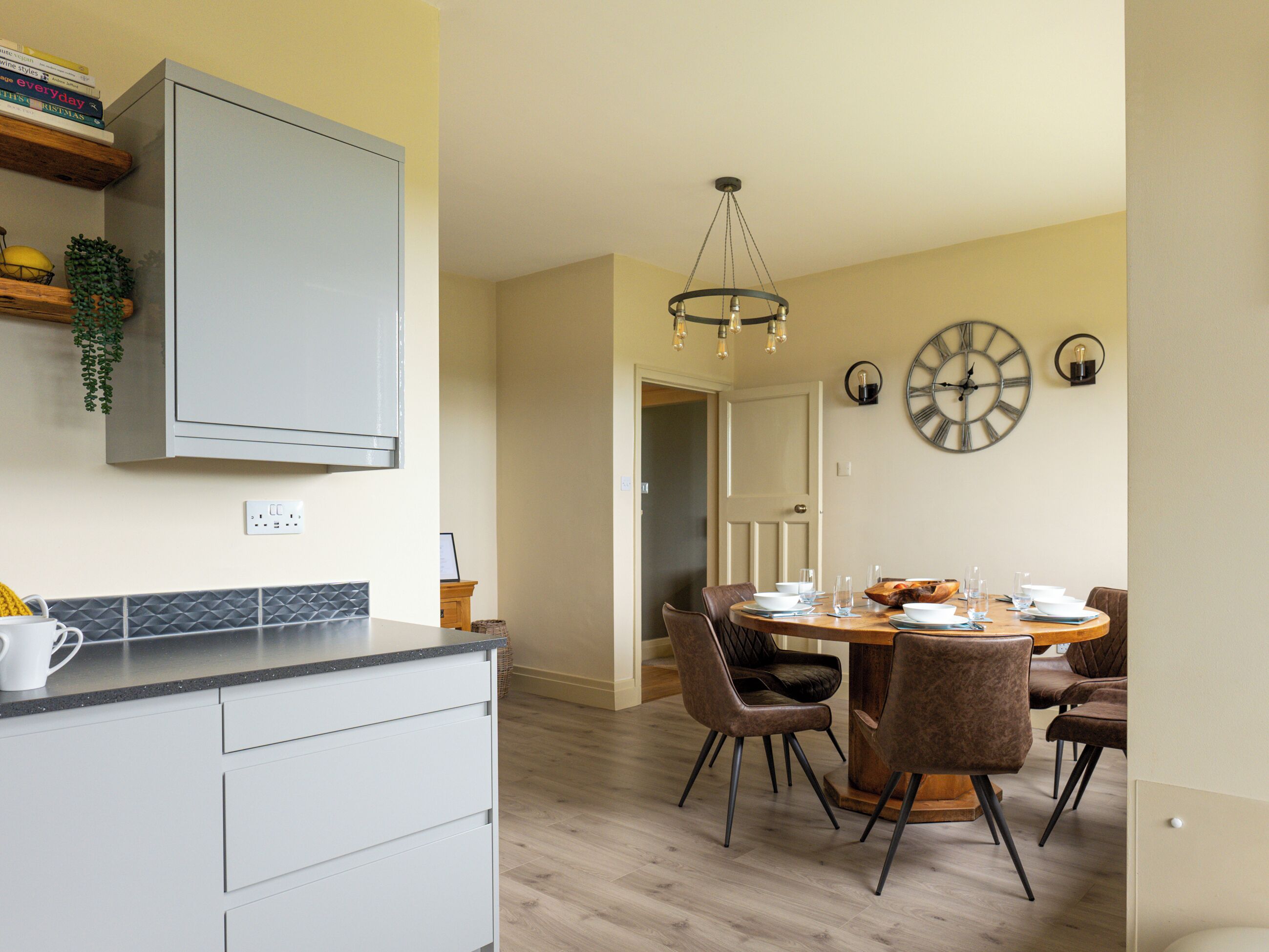 Una cocina moderna con horno empotrado, un comedor con mesa y sillas de madera, y un reloj de pared grande.