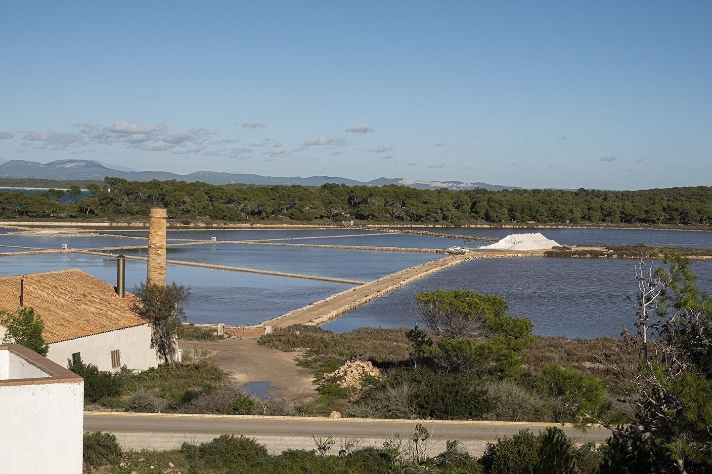 Un paysage côtier avec des marais salants, une route et un bâtiment doté d’une cheminée.