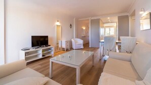 A modern living room with a glass coffee table, white sofas, a TV, and a white armchair. - Exclusive holiday apartment in Colonia Sant Jordi for max. 4 people (Colonia Sant Jordi)