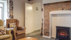 A cozy living room with a fireplace, a sofa, a wooden table, and a door leading to another room. - Set in the picturesque border town of Montgomery, close to all town amenities. (Montgomery, near Welshpool)