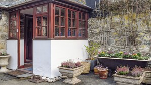 A traditional stone building with a corner windowed structure, potted plants, and a stone wall. - Set in the picturesque border town of Montgomery, close to all town amenities. (Montgomery, near Welshpool)