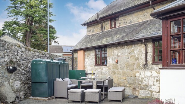 A stone building with a patio area featuring wicker furniture and potted plants. - Set in the picturesque border town of Montgomery, close to all town amenities. (Montgomery, near Welshpool)