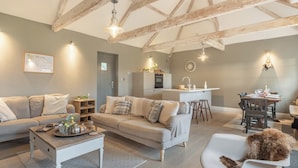 A spacious living area with a high ceiling, exposed wooden beams, a dining area with a central island, and a cozy seating arrangement. - 2 bedroom accommodation in Northrepps (Northrepps)