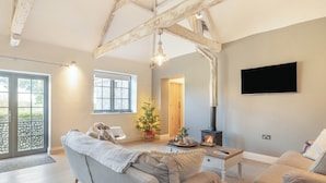 A cozy living room with a fireplace, a sofa, a coffee table, and a TV mounted on the wall. - 2 bedroom accommodation in Northrepps (Northrepps)