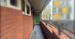 A narrow corridor with a brick wall on one side and a metal railing on the other. A green door is visible in the distance. - Spacious 3BD Duplex Steps from Old Street Station (London)