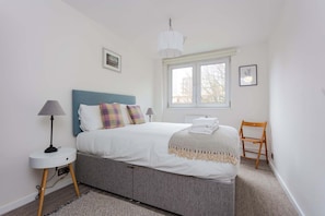 A bedroom with a bed, a bedside table with a lamp, a chair, and a window. - Spacious 3BD Duplex Steps from Old Street Station (London)