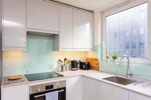 Una cocina moderna con armarios blancos, un lavamanos de acero inoxidable, una tetera y un tostador.