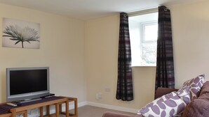 A living room with a TV on a wooden table, a couch with patterned cushions, and a window with striped curtains. - The Coach House Halifax (Halifax)
