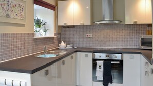 A modern kitchen with a built-in oven, a microwave, and a window with a view of plants. - The Coach House Halifax (Halifax)